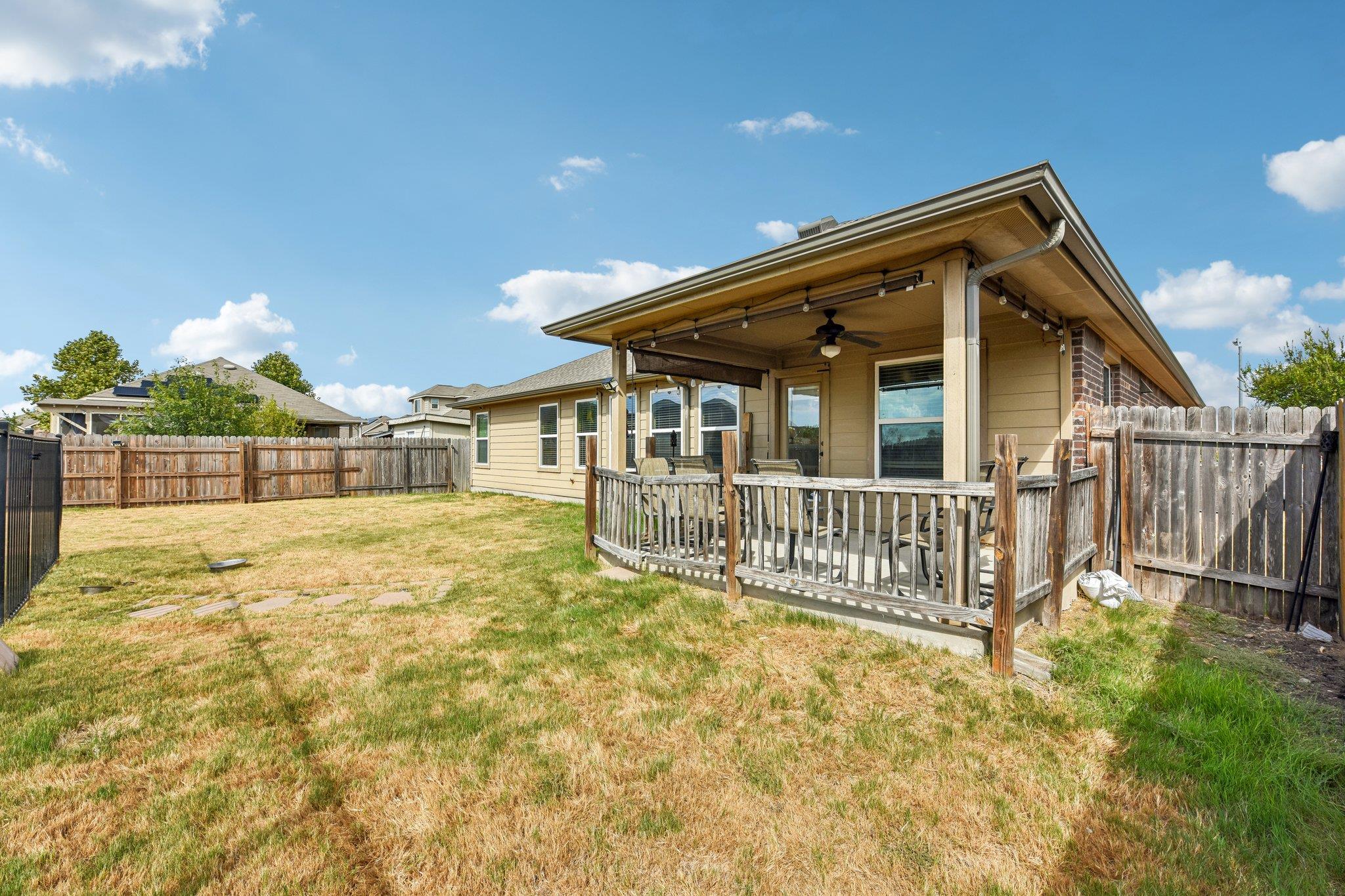 Home’s covered back patio with outdoor seating and a spacious fenced yard.