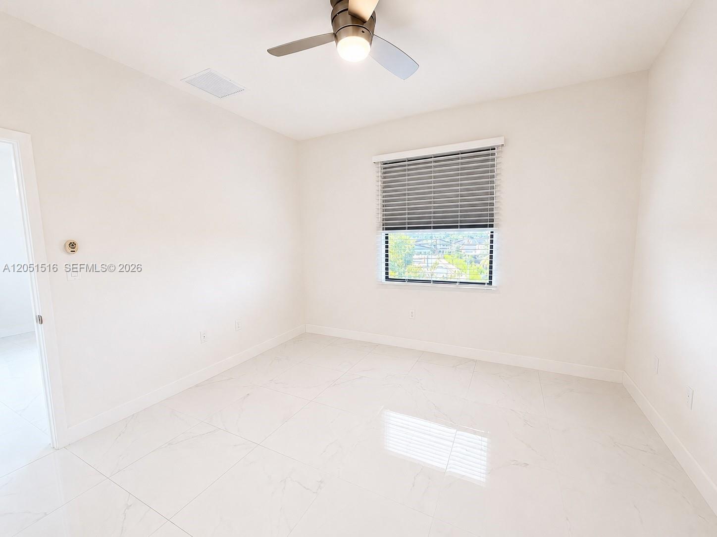Empty bright room with glossy tile floors, a ceiling fan, and a window with horizontal blinds.