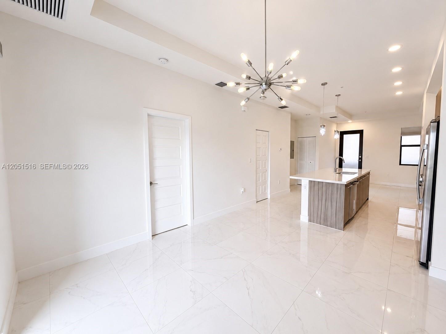 Unfurnished kitchen with a wood-finish island, glossy tile floors, and a starburst chandelier.