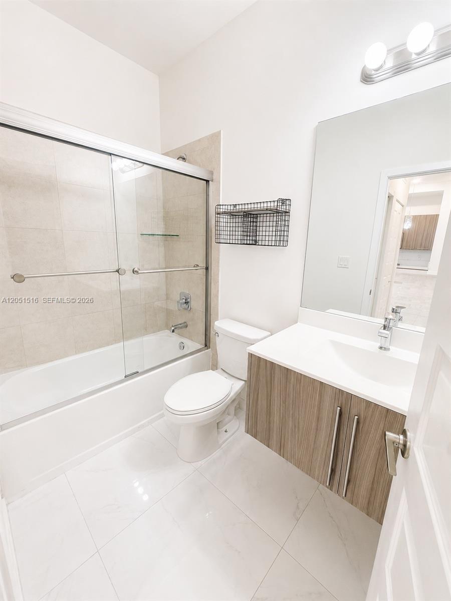 Bathroom with a glass-enclosed tub, beige tile, and wood-grain vanity.