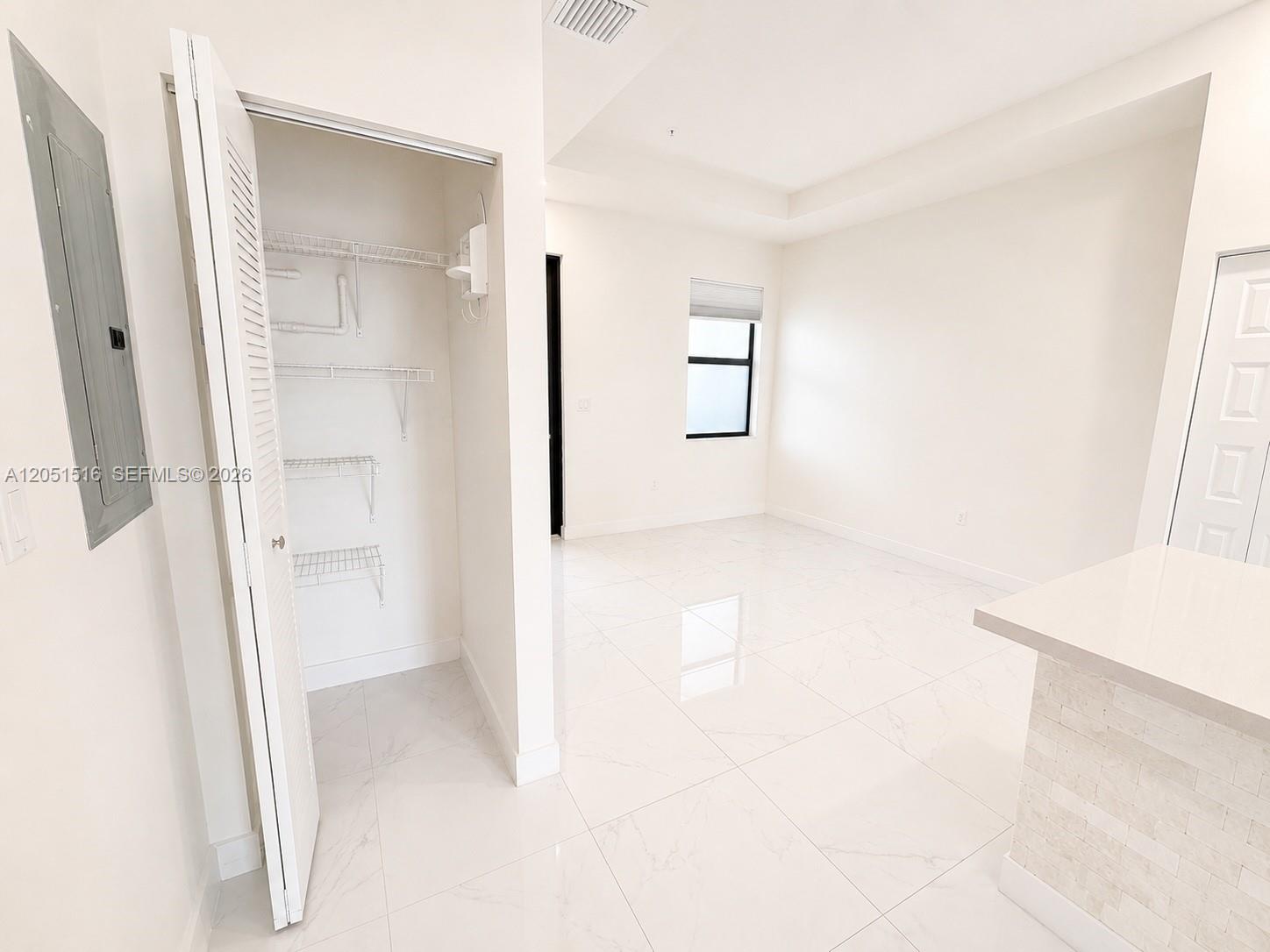 Vacant room with glossy white tile floors, an open wire-shelved closet, and a small window.