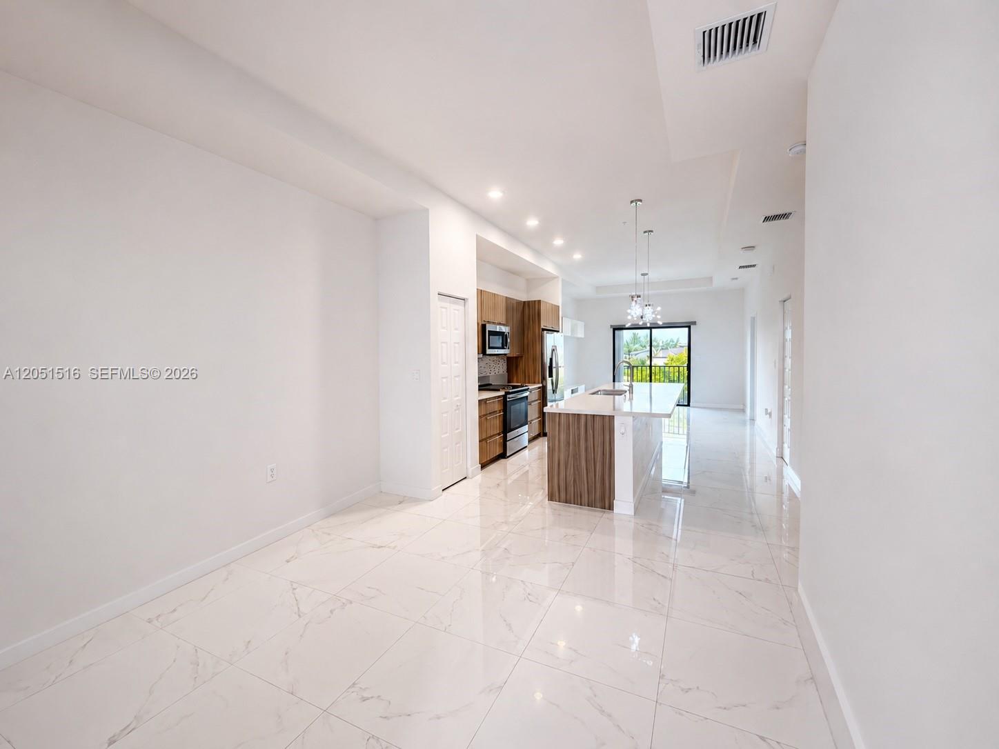 Open-plan kitchen with wood cabinetry, a large island, glossy tile floors, and sliding doors to a balcony.