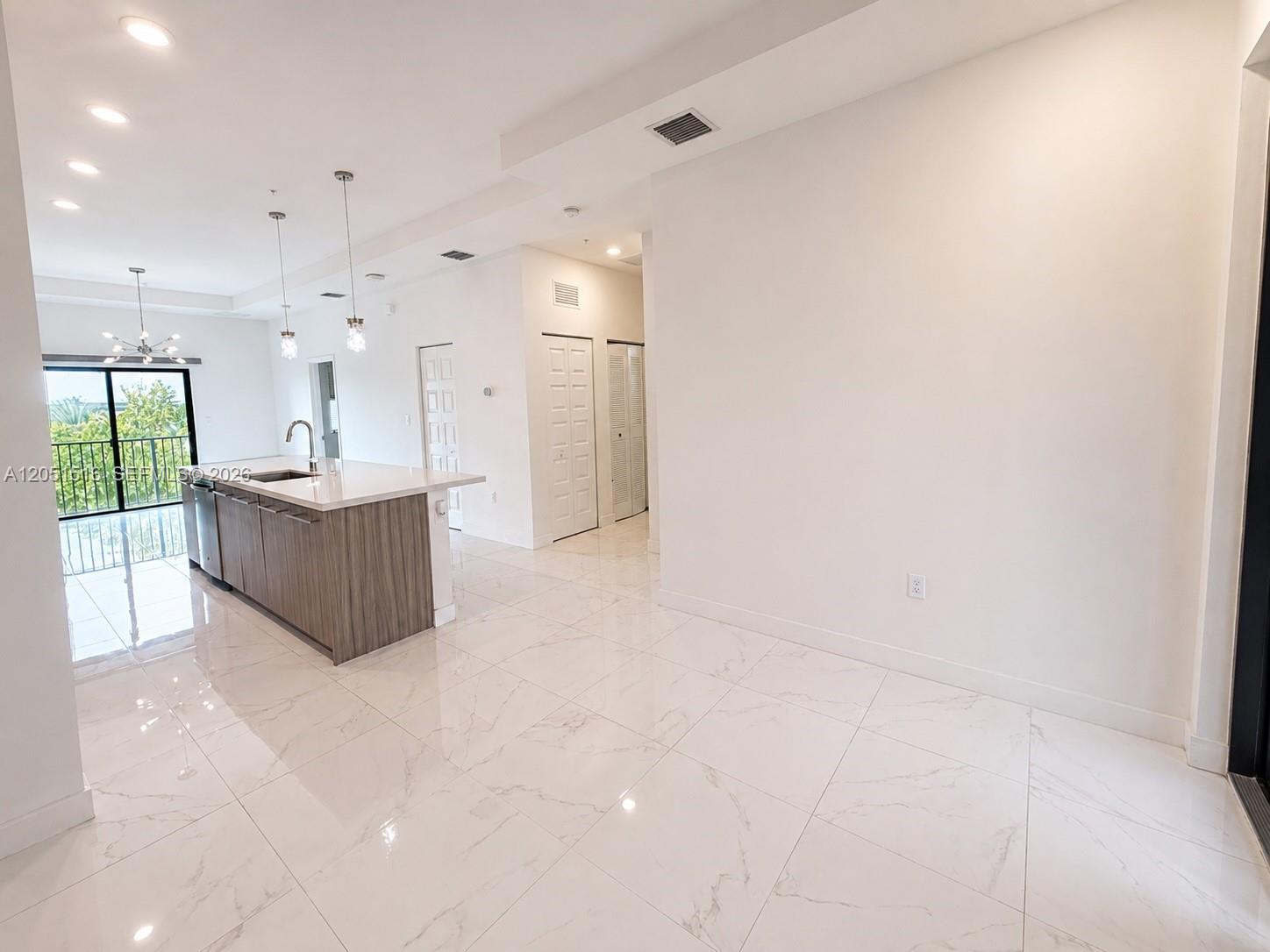 Open-plan kitchen with a wood-grain island, glossy tile floors, and balcony doors overlooking greenery.