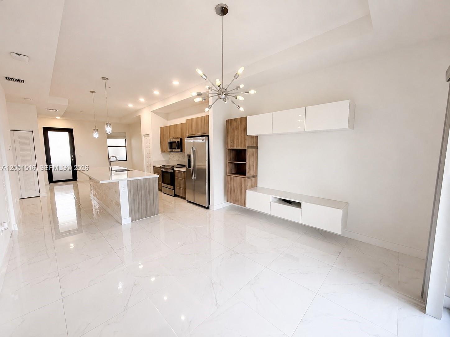 Open-plan kitchen and living area with a white island, wood cabinetry, and glossy tile floors.