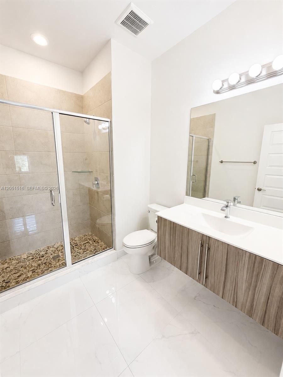 Bathroom with a glass-enclosed shower, pebble floor, and wood-grain vanity.
