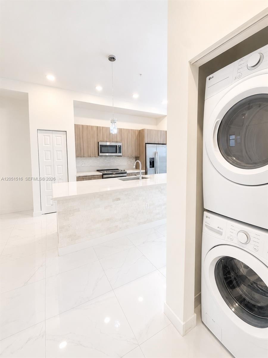 Bright kitchen with a white stone island and wood cabinets beside a recessed stacked washer and dryer.