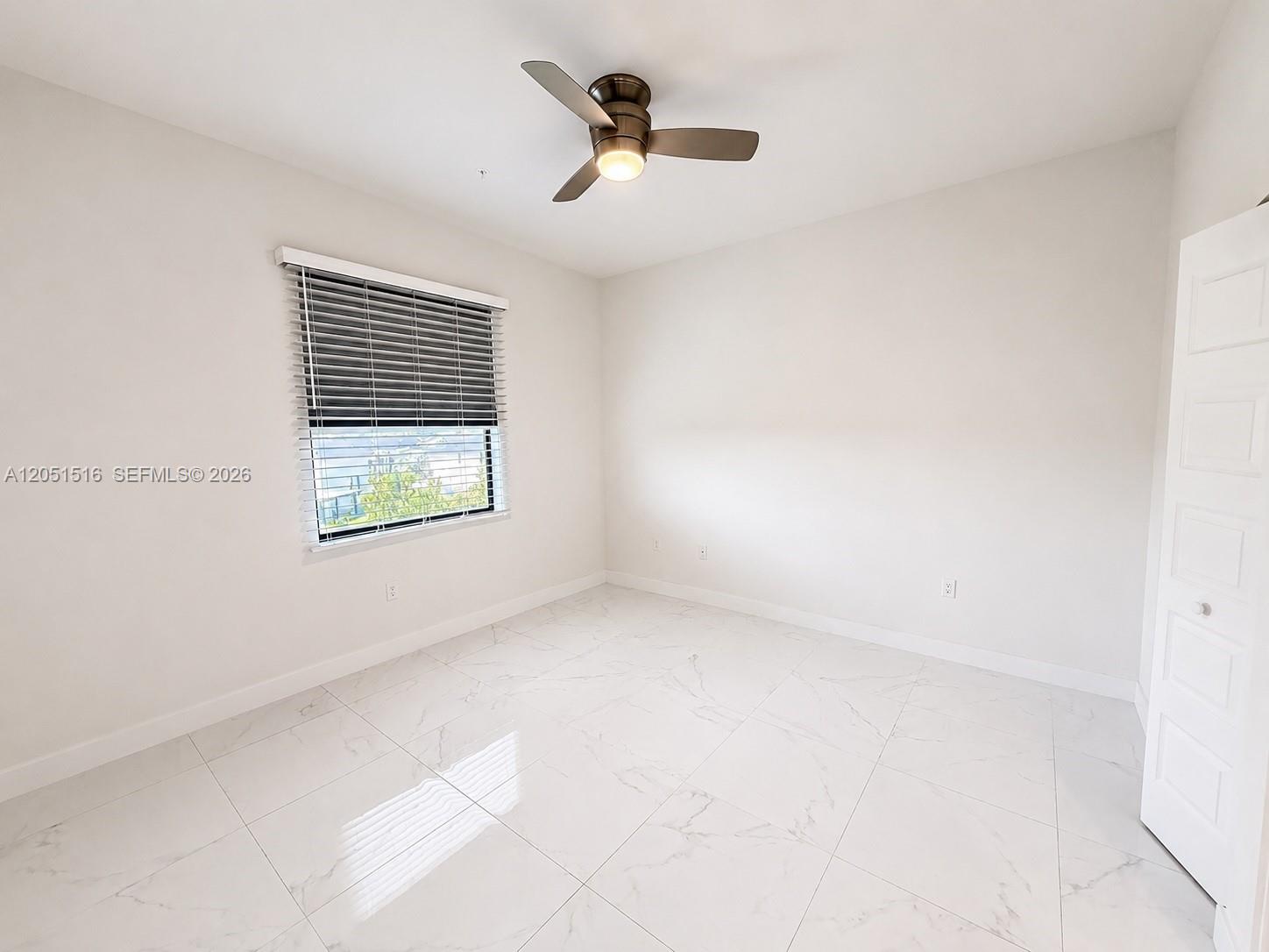 Empty room with glossy marble-look tile, a ceiling fan, and a window with blinds.