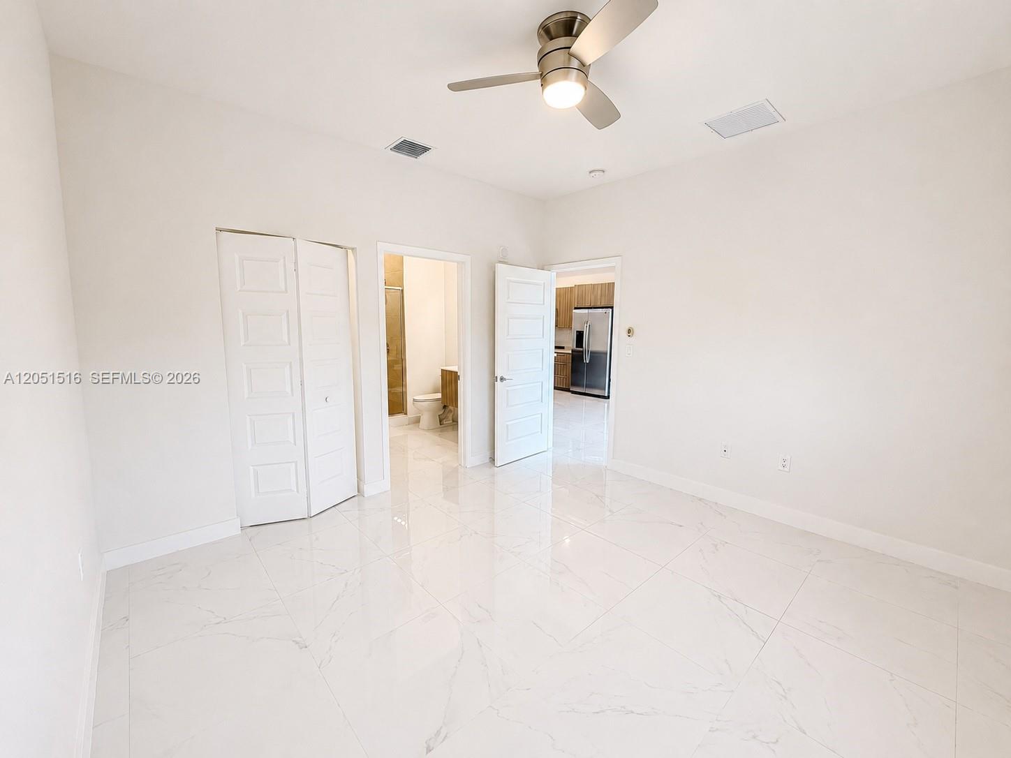 Empty bedroom with glossy tile floors, a ceiling fan, and open views into the bathroom and kitchen.
