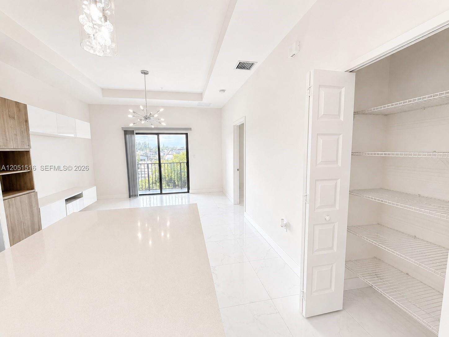 Open kitchen and living area with white tile floors, a broad countertop, and an open pantry with wire shelves.