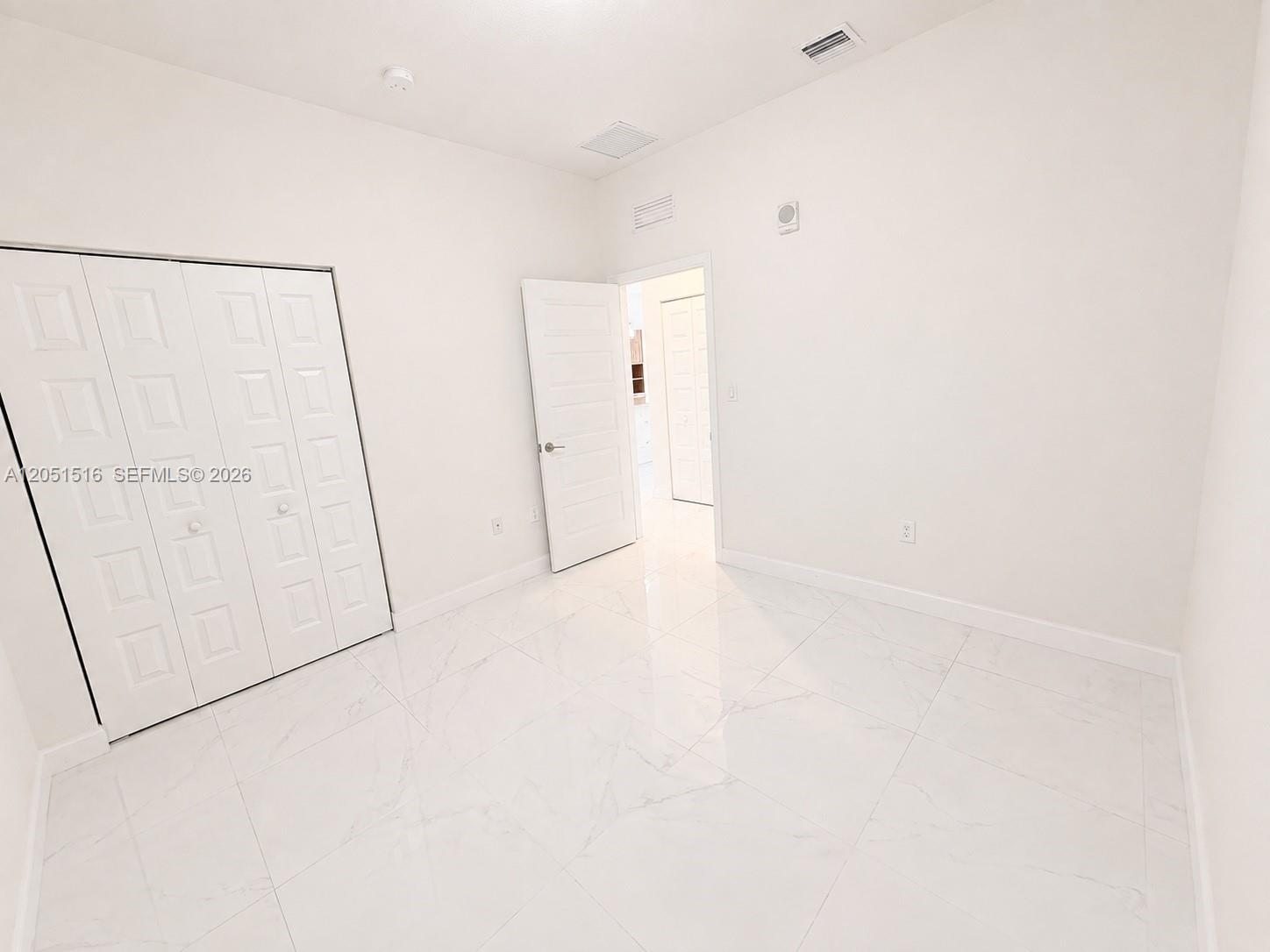 Empty room with glossy marble-pattern tile floors and a folding closet door.