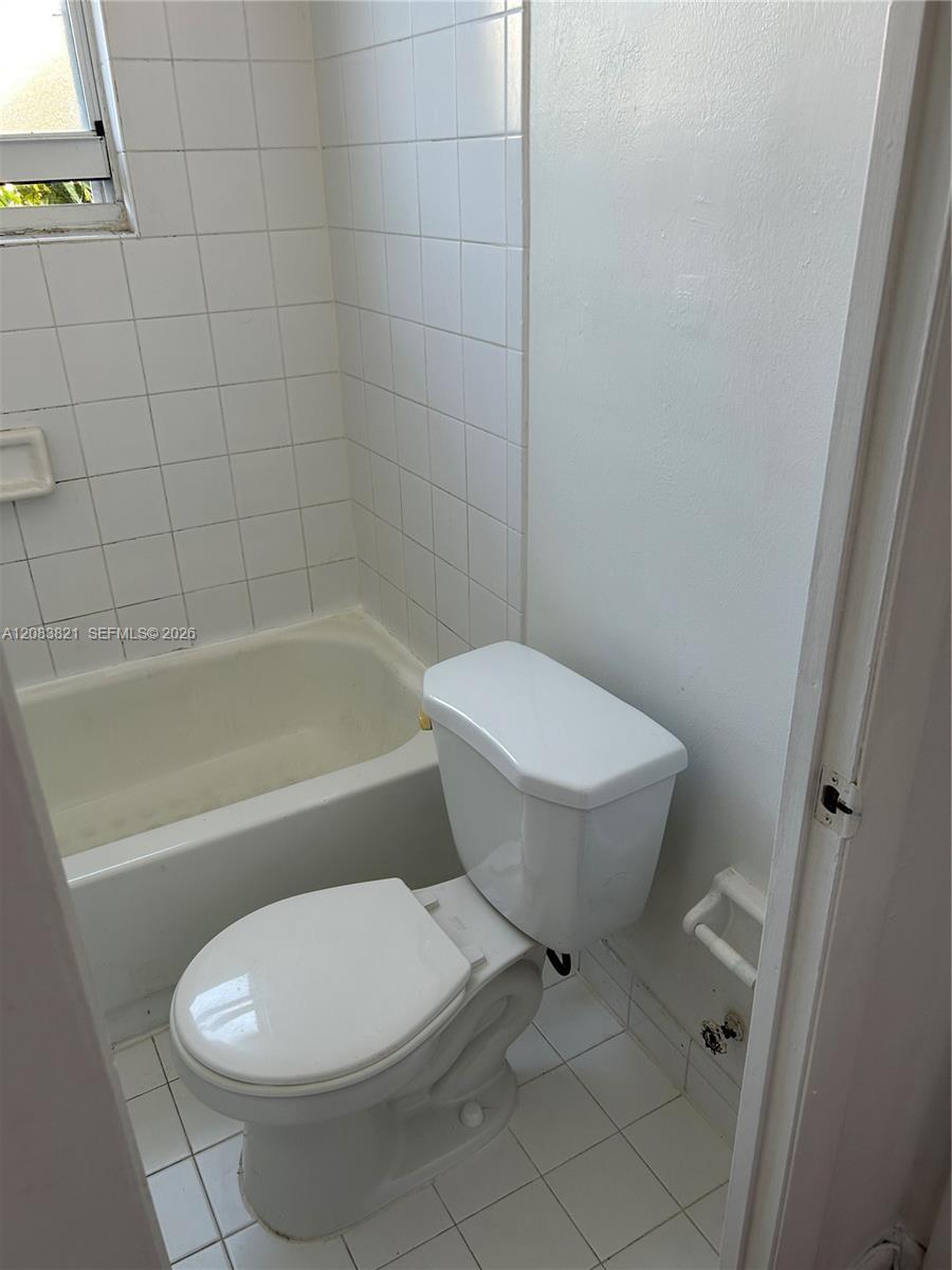 Bathroom with a white bathtub and toilet, tiled walls, and a high window.