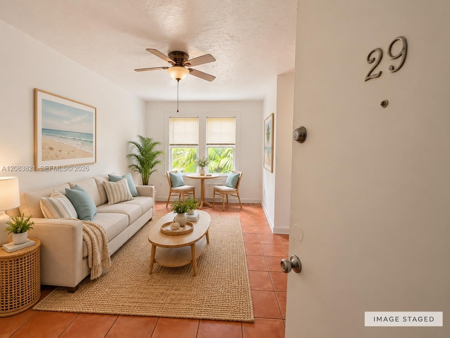Staged living room with a cream sofa, terracotta tile, and dining table beside two windows.