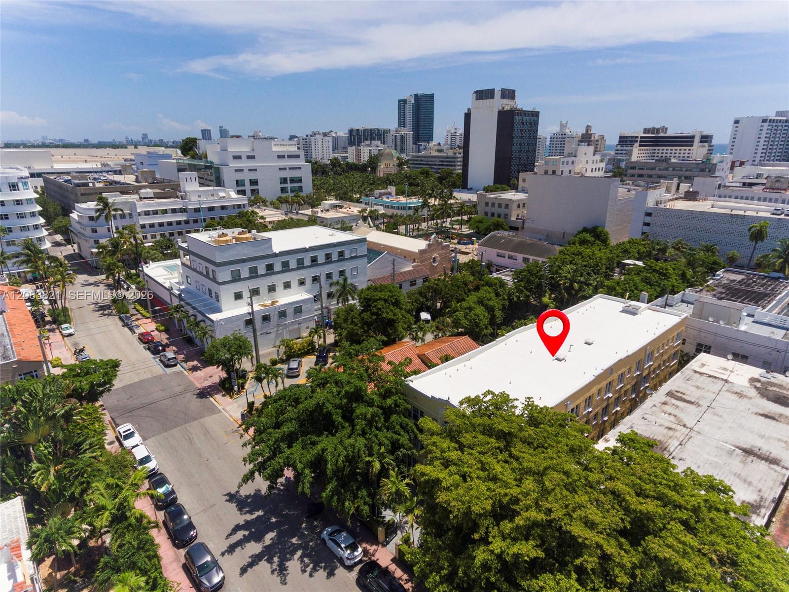 Aerial view of a Miami Beach neighborhood, with a red pin marking a white-roofed building among palm trees and city buildings.
