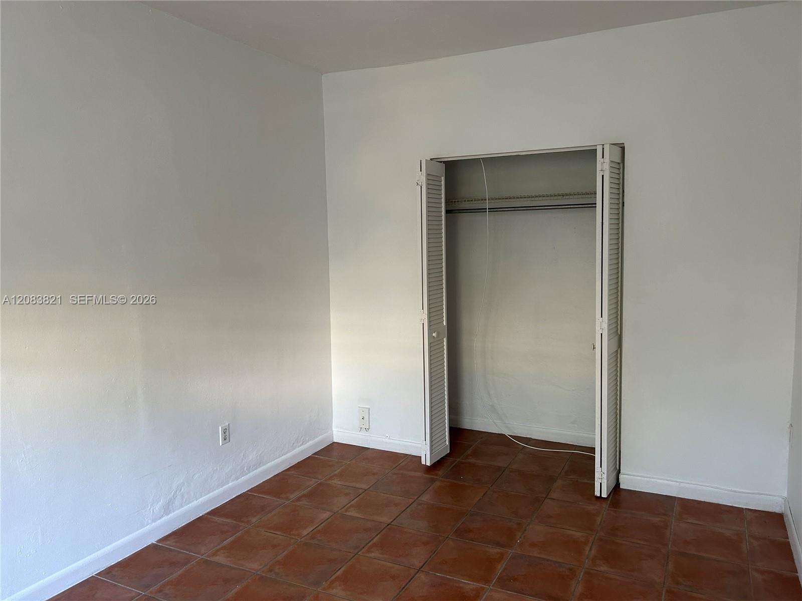 Empty bedroom with terracotta tile flooring and an open louvered closet.