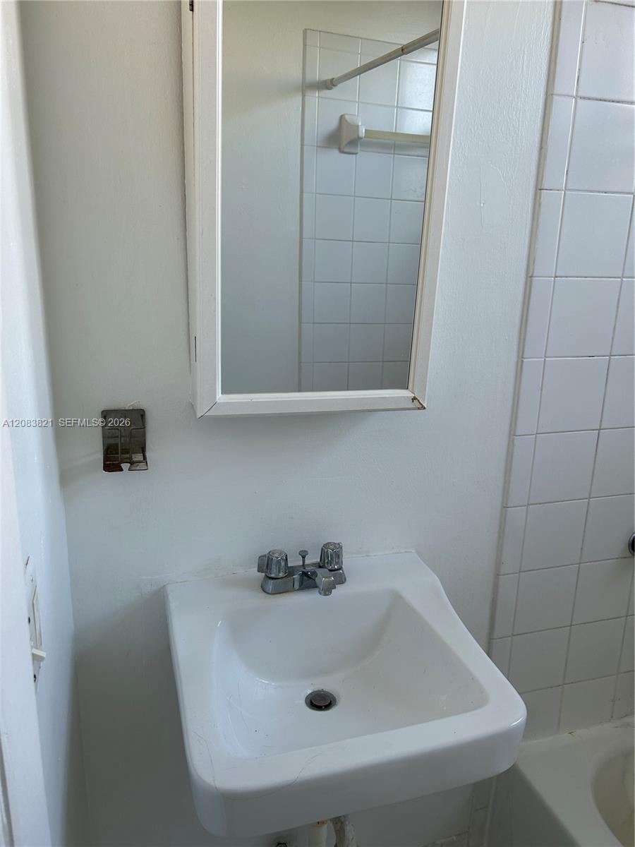 Bathroom with a wall-mounted sink, rectangular mirror, and white-tiled shower area.