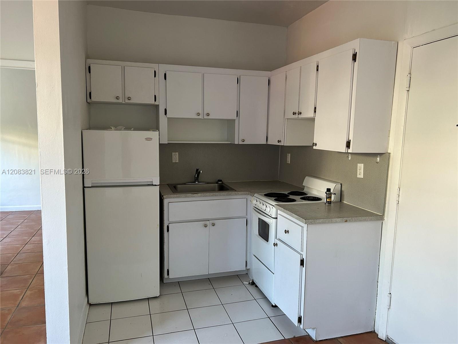 Vacant kitchen with white cabinets, a refrigerator, and an electric stove.