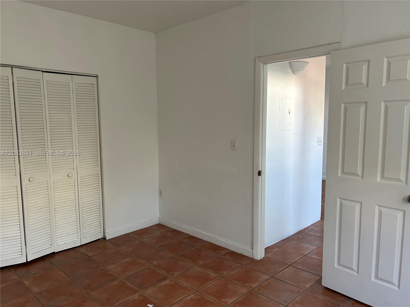 Empty bedroom with terracotta tile floors, louvered closet doors, and an open doorway.
