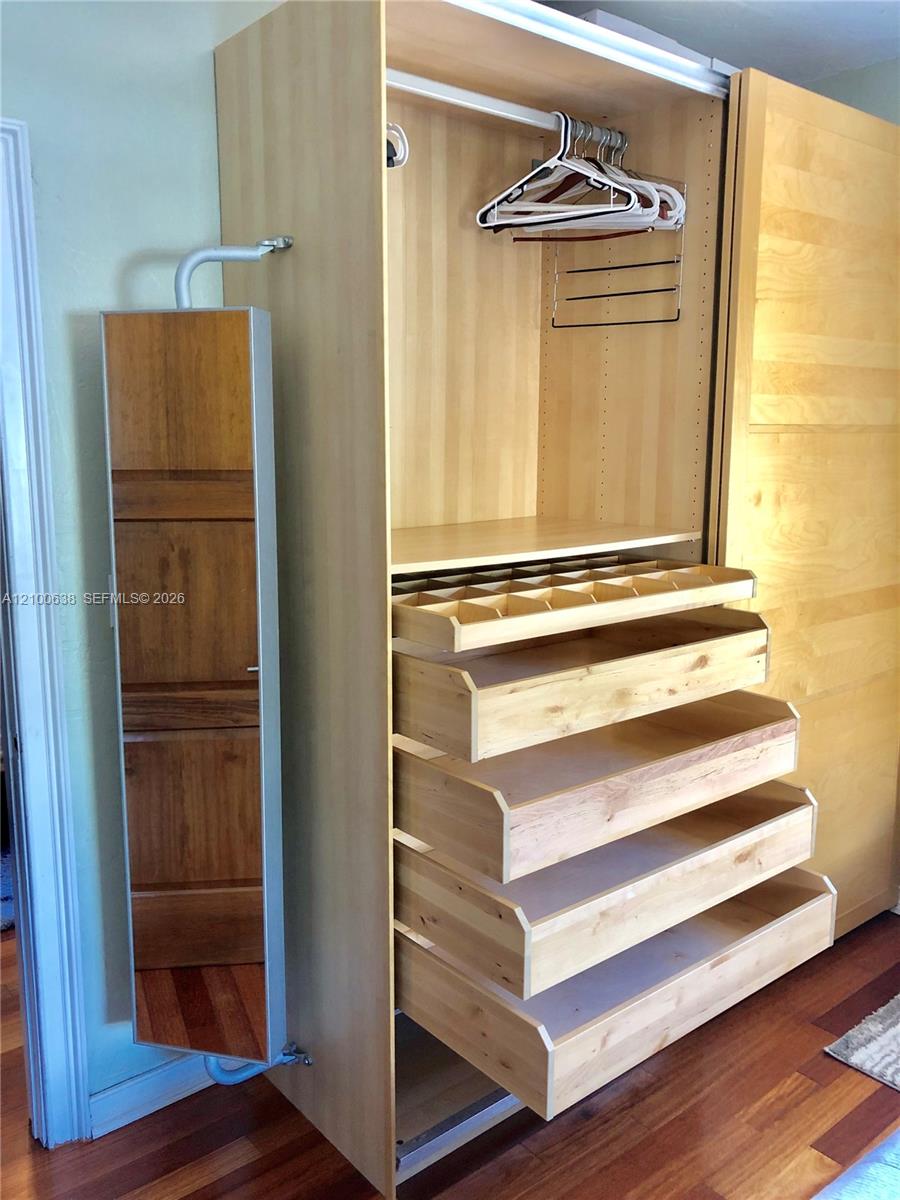 Built-in light wood wardrobe with open drawers, hangers, and a narrow mirrored door.