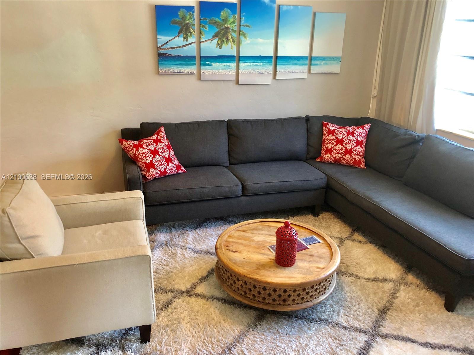 Furnished living room with a gray sectional, red pillows, and round wooden coffee table.