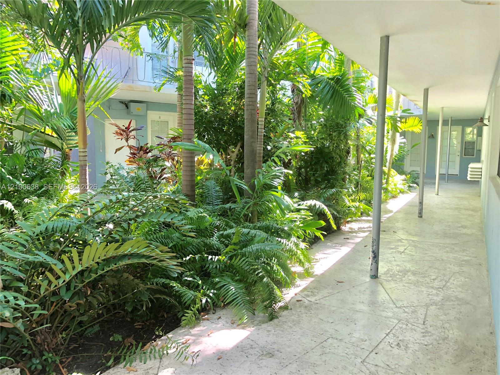 Tropical landscaped courtyard walkway beside a light-blue residential building.