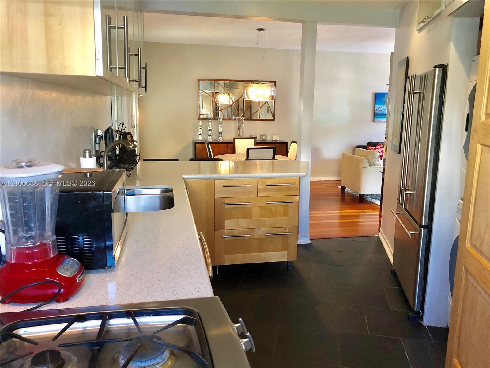 Kitchen with a light wood island and stainless steel refrigerator, opening to a dining area and living room.