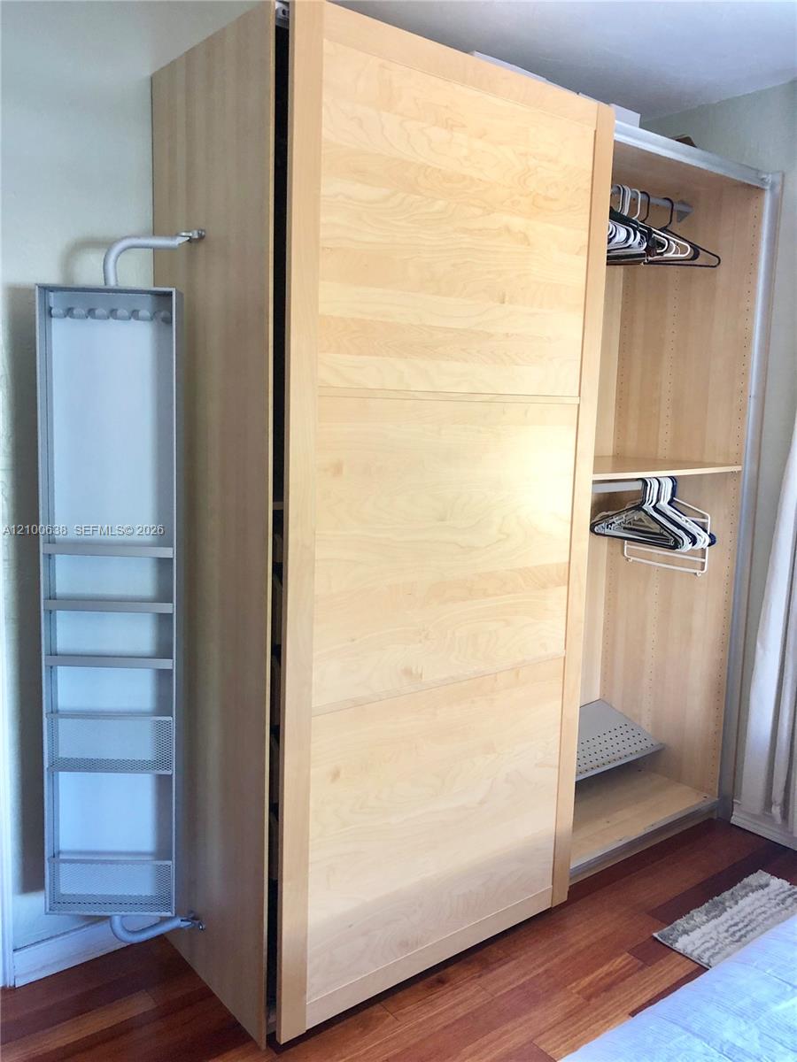 Light wood bedroom closet with sliding doors, open shelves, hangers, and a pull-out organizer.