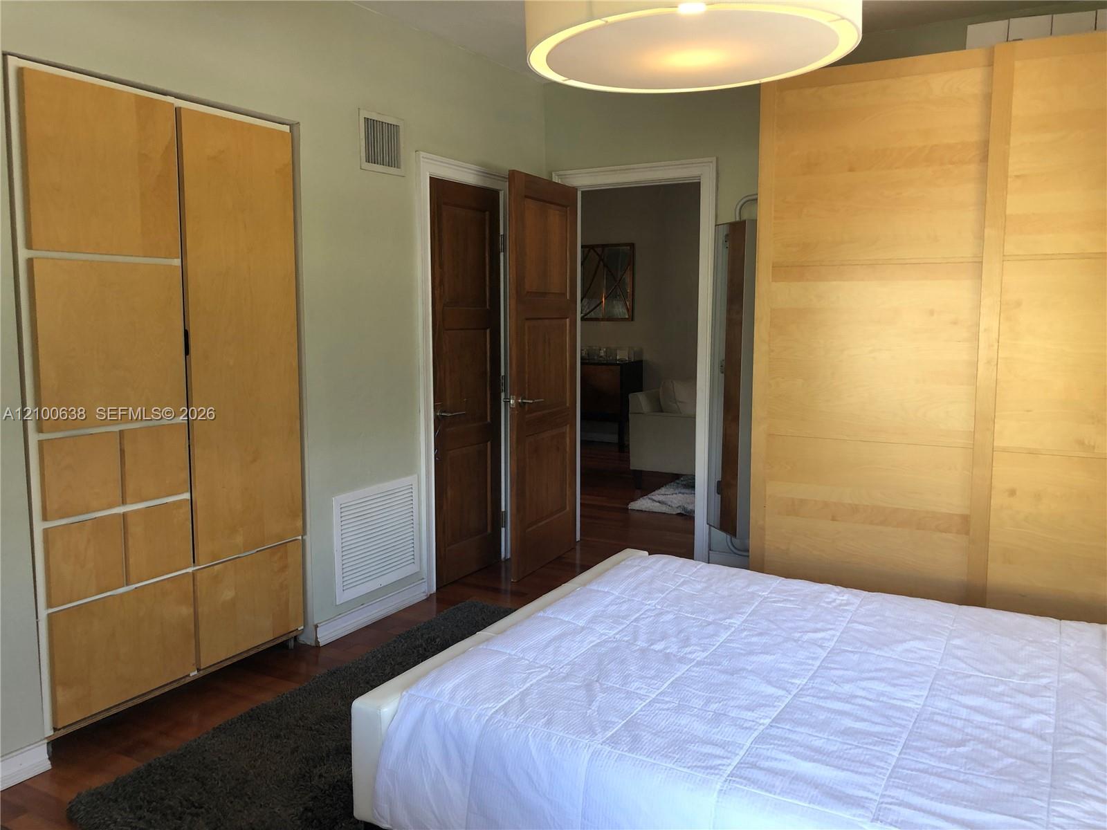 Bedroom with honey-colored built-in wardrobes, dark wood flooring, and a white bed.
