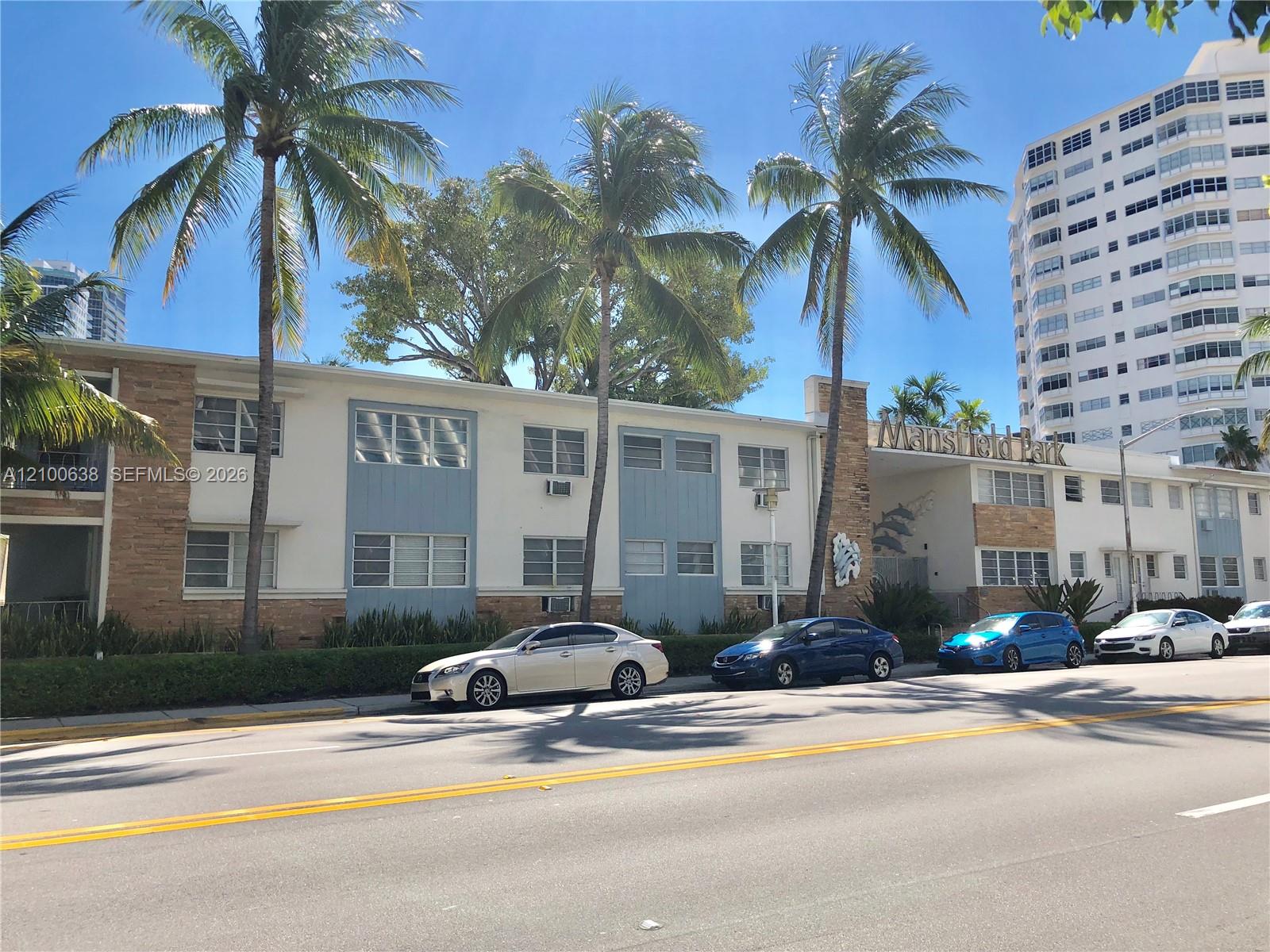 Mansfield Park apartment building with palm trees and parked cars along the street.