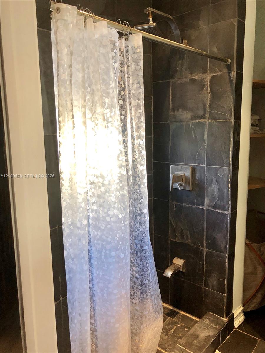 Bathroom shower with dark stone tile and a white pebble-pattern curtain.