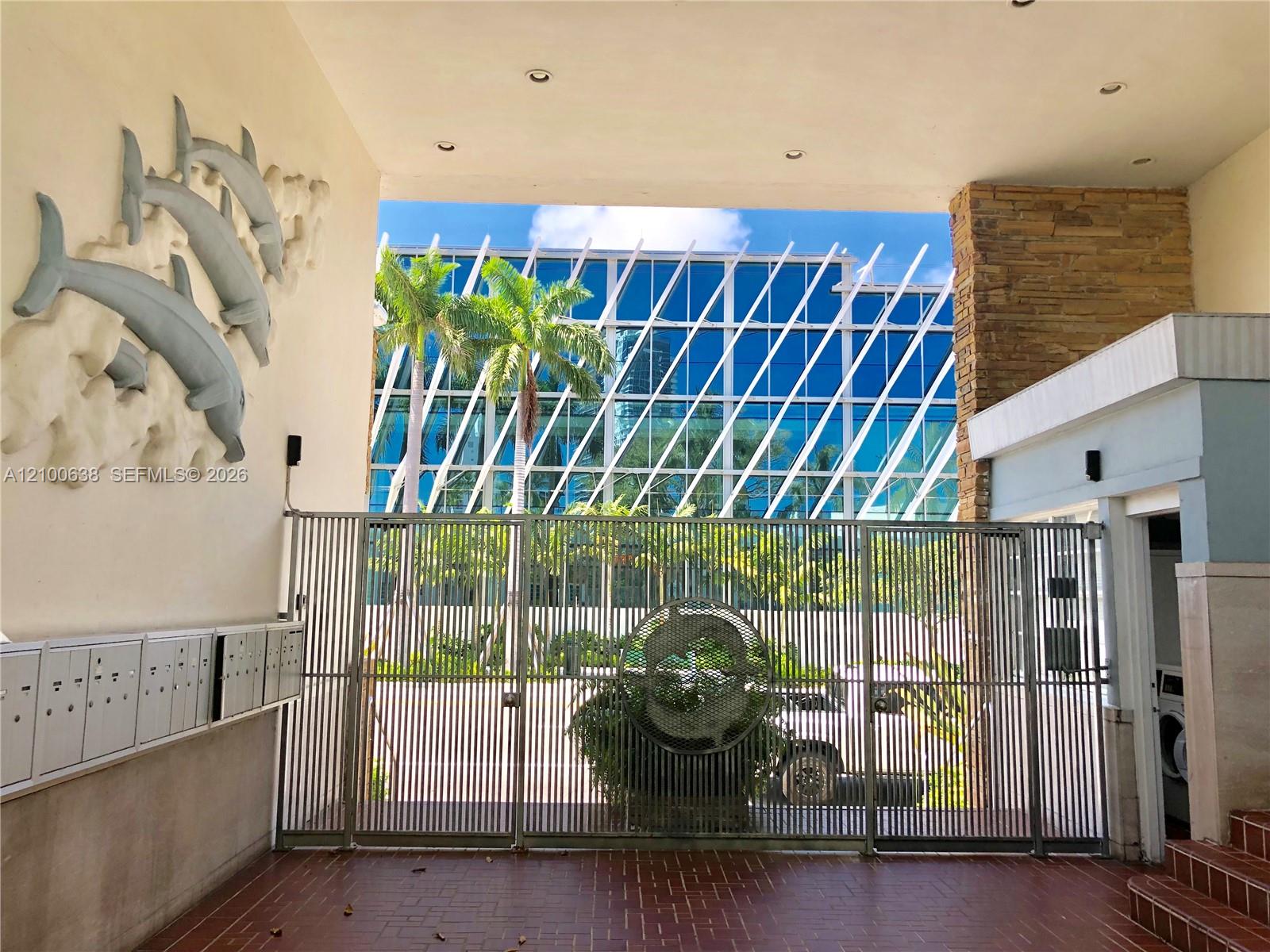 Covered building entrance with a metal gate, mailboxes, and a sculptural wall feature.