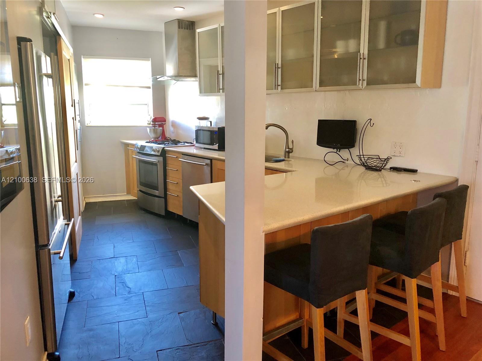 Kitchen with stainless steel appliances, dark tile flooring, and a breakfast bar with stools.