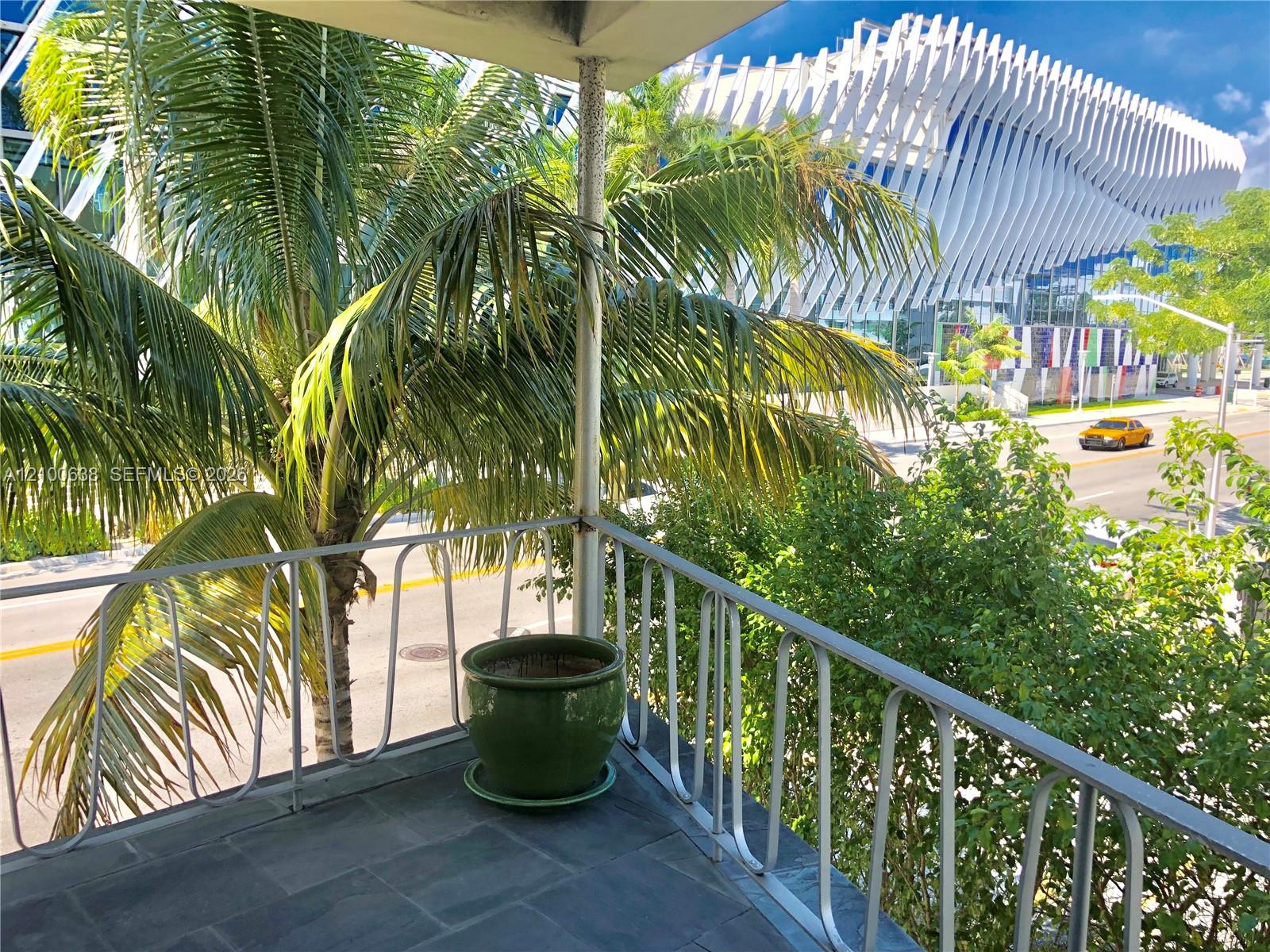 Apartment balcony overlooking palm trees, a street, and a striking white modern building.