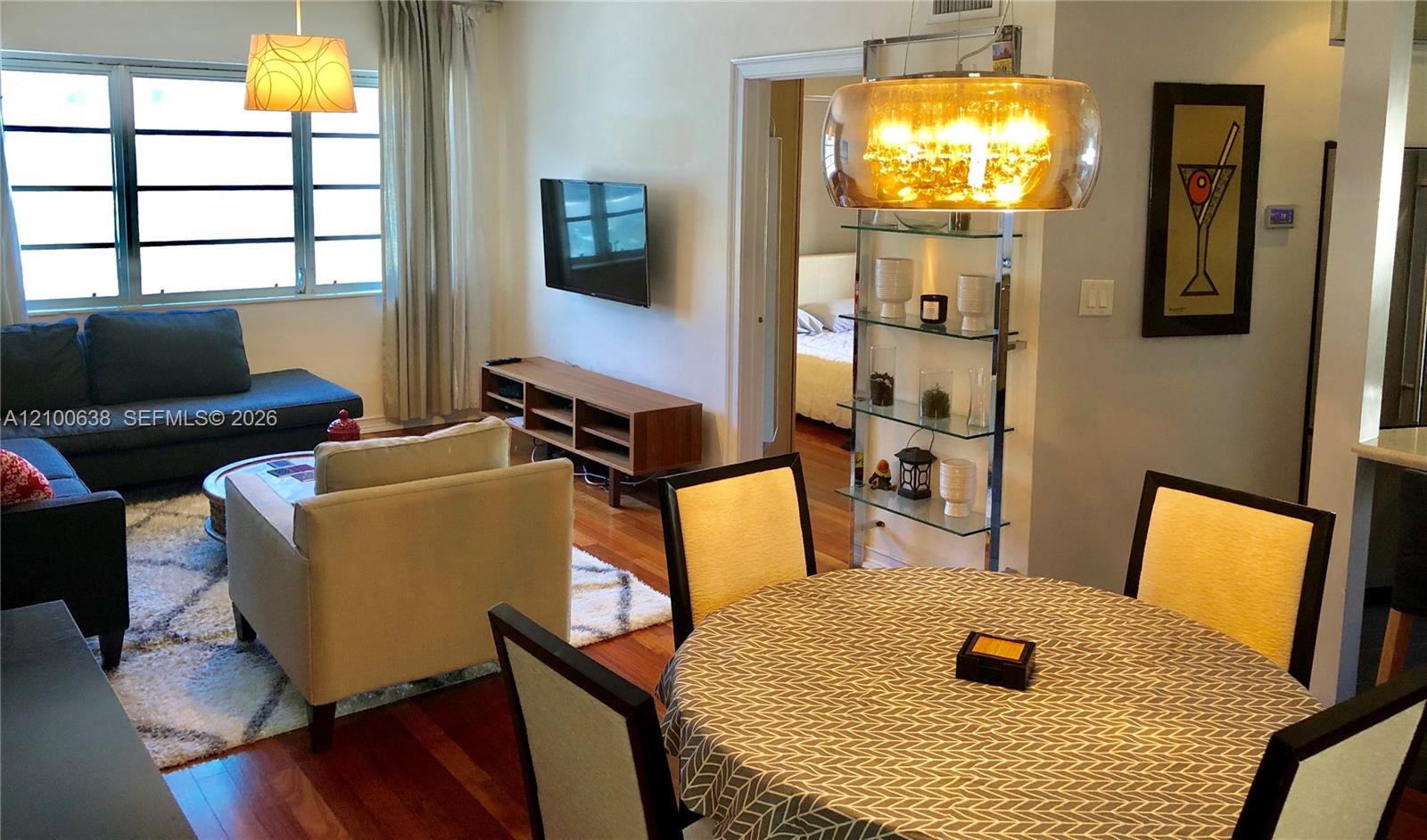 Furnished living and dining area with hardwood floors, blue sofa, and large windows.