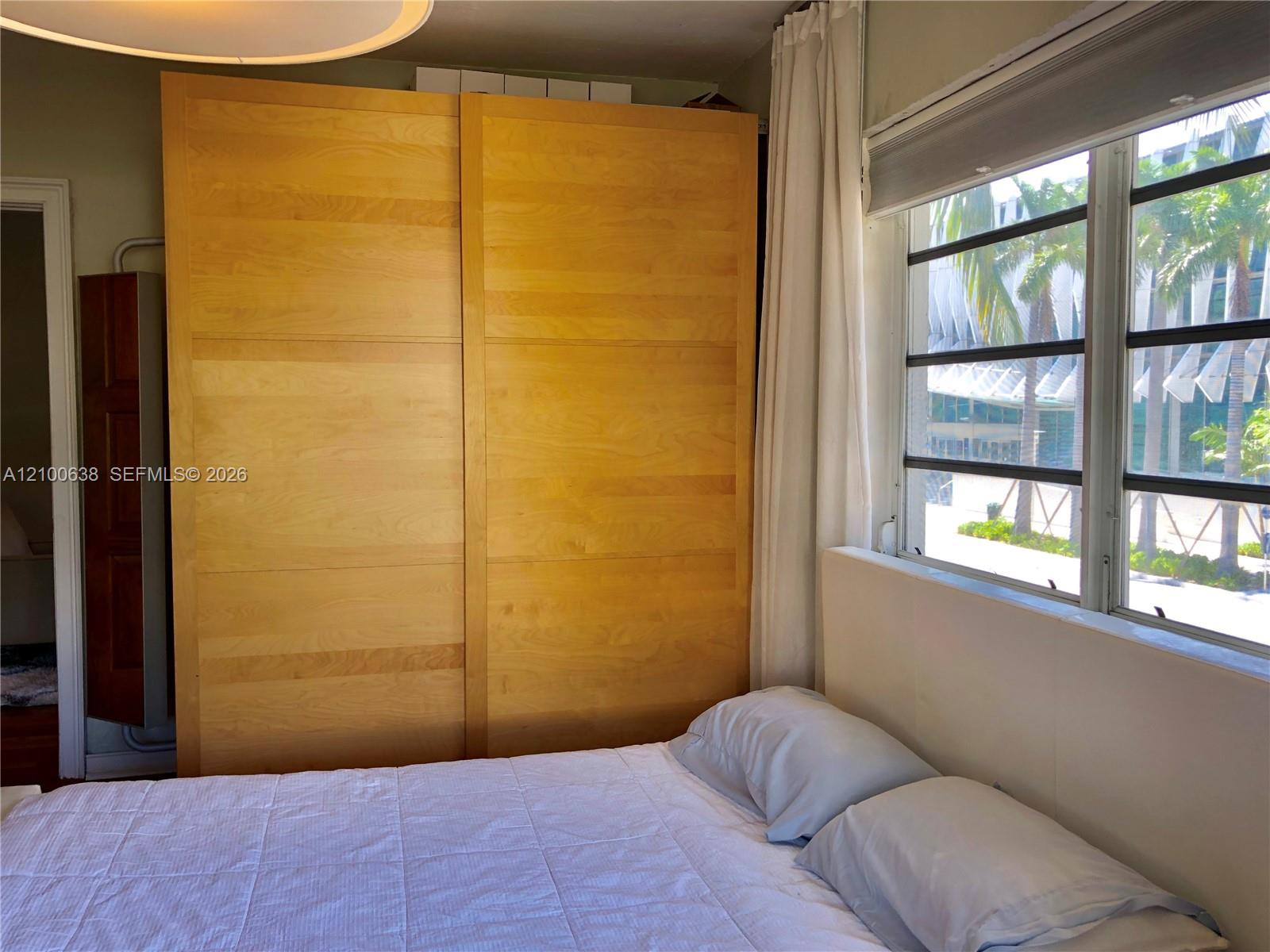 Bedroom with a large light-wood sliding wardrobe and wide windows overlooking palm trees.