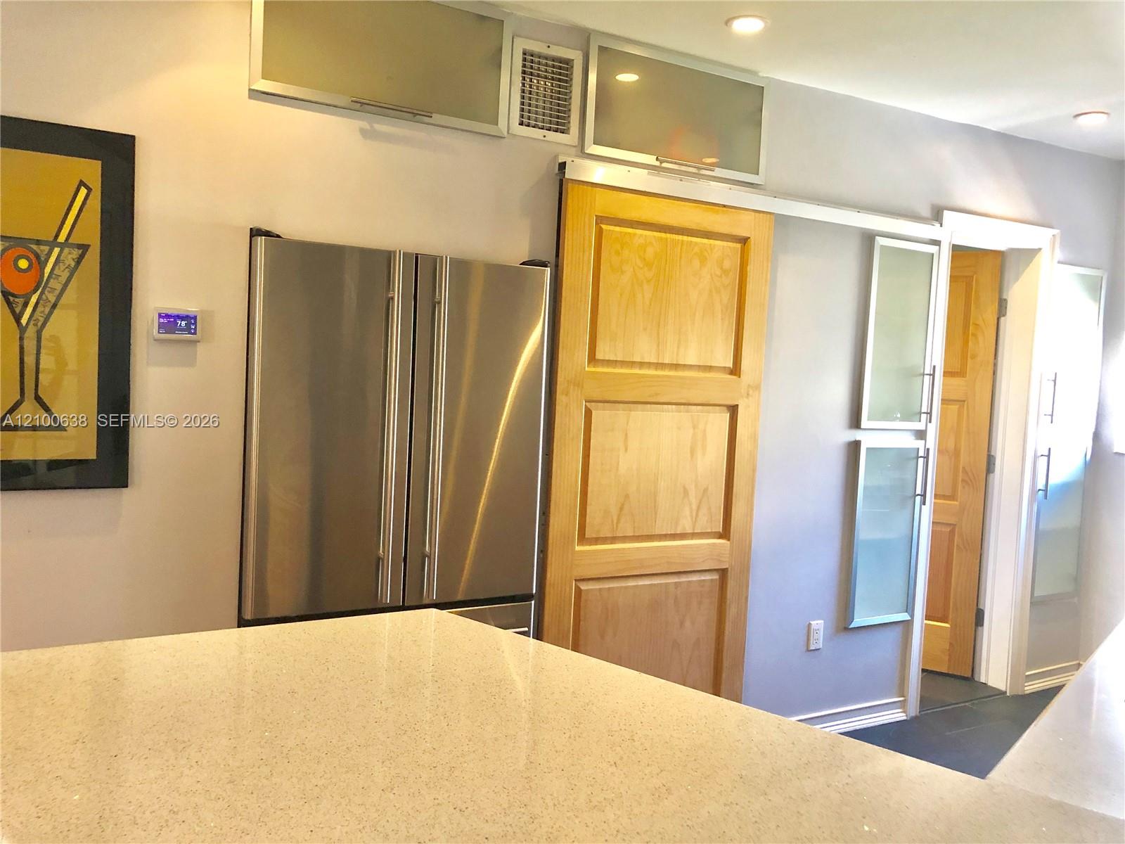 Kitchen with a pale speckled countertop, stainless steel refrigerator, and light wood cabinetry.