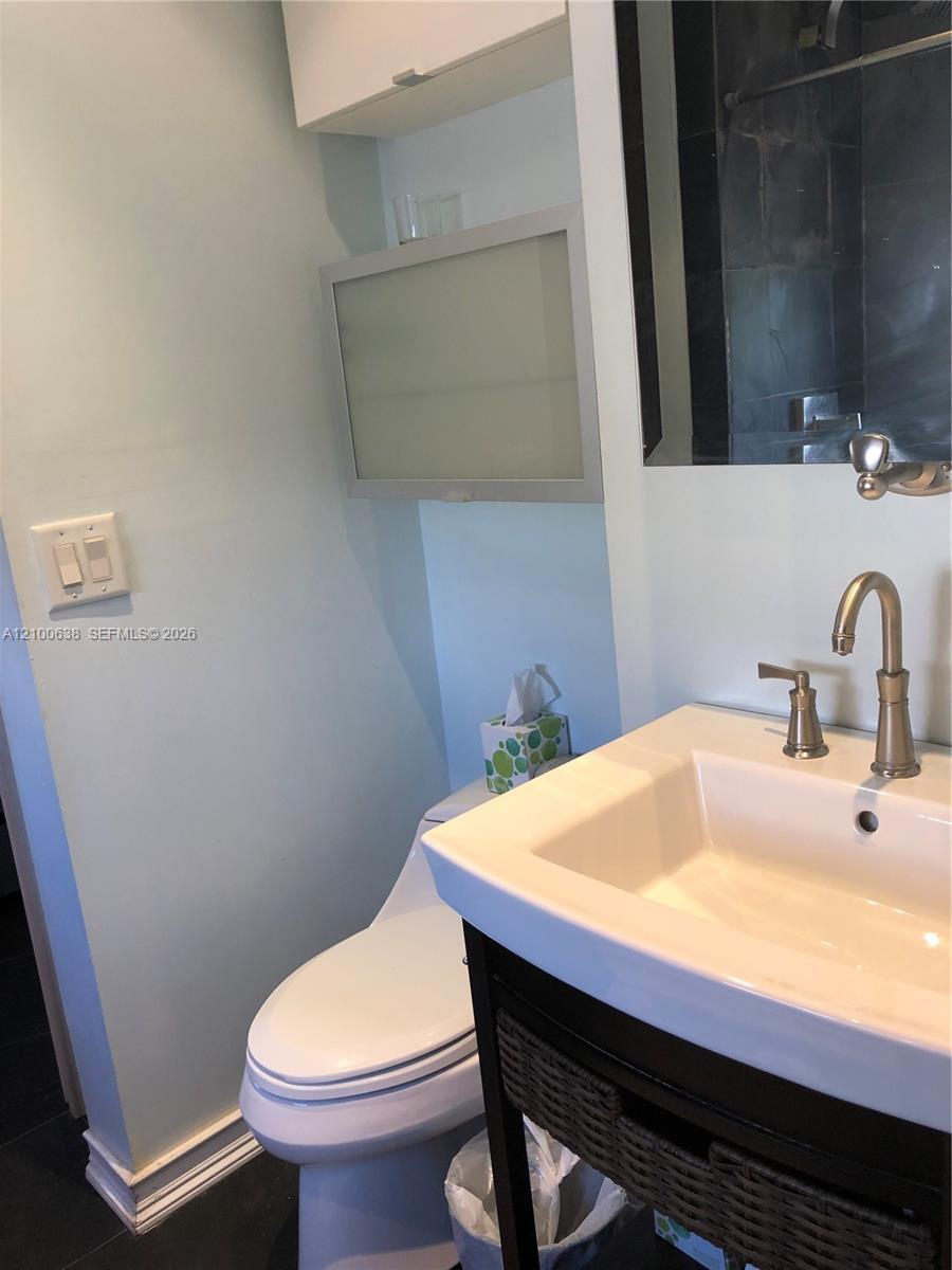Compact bathroom with a white sink and dark vanity beside a toilet and mirrored medicine cabinet.