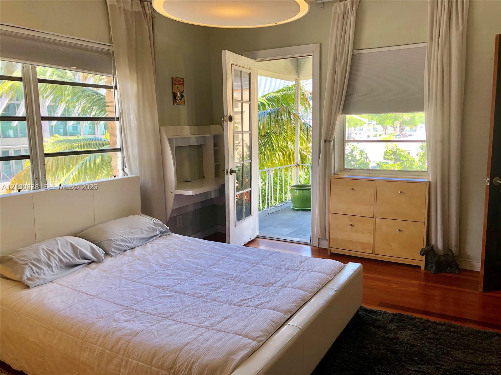 Bedroom with hardwood floors and an open balcony door framed by palm trees.