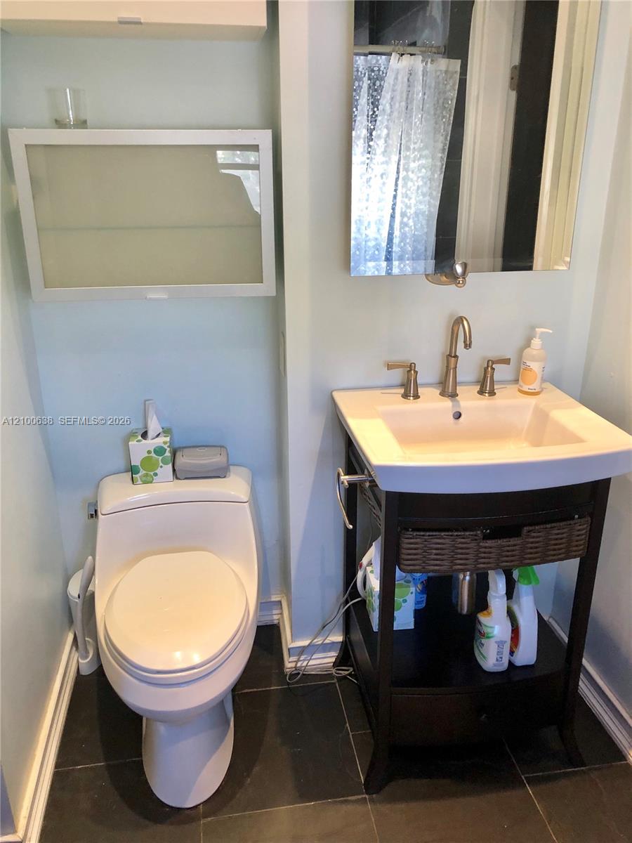 Bathroom with a white toilet, dark wood vanity, large mirror, and dark tile floor.