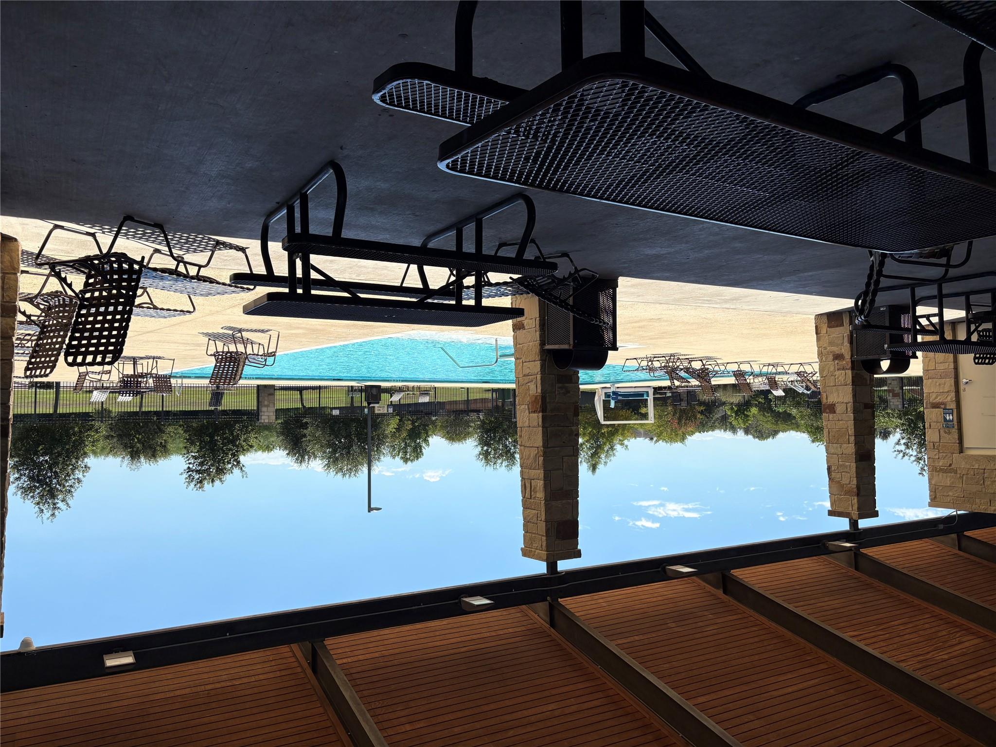 Community pool with lounge chairs beside a covered pavilion with stone columns and picnic tables.