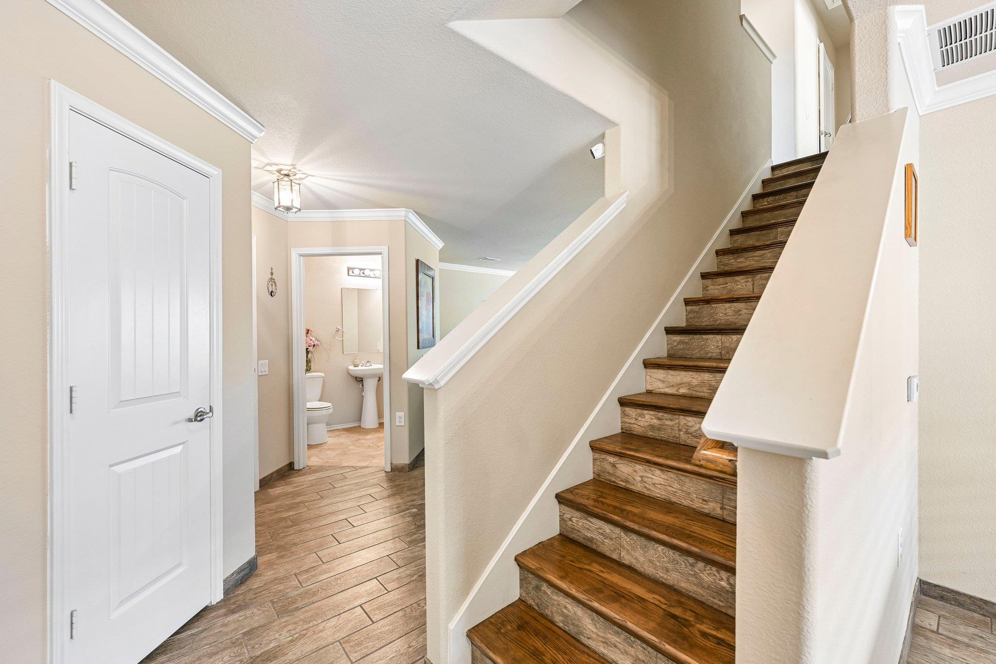Entry hall with dark wood stairs, wood-look tile flooring, and an open doorway to a powder room.