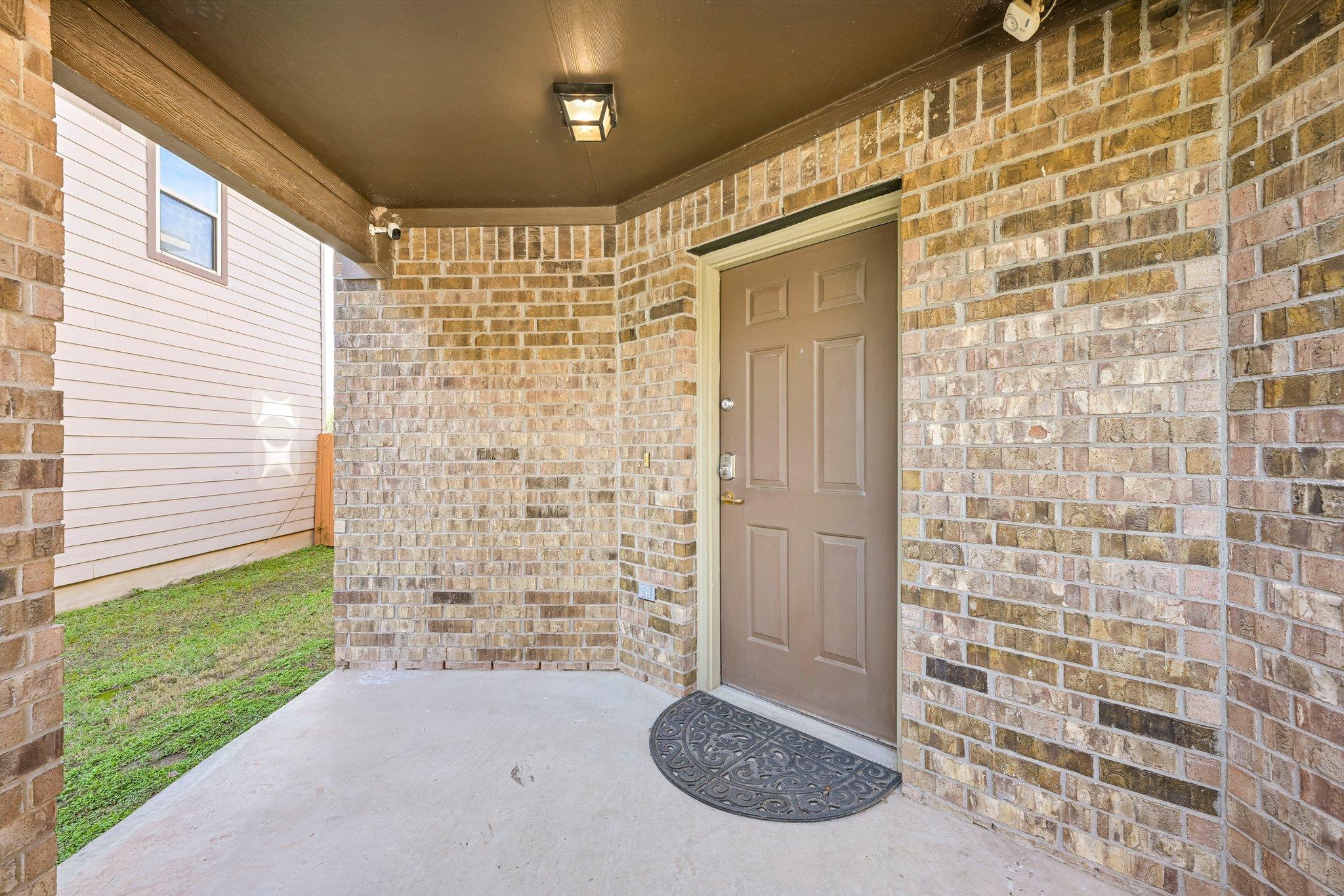Covered brick entry porch with a brown front door and semicircular doormat.