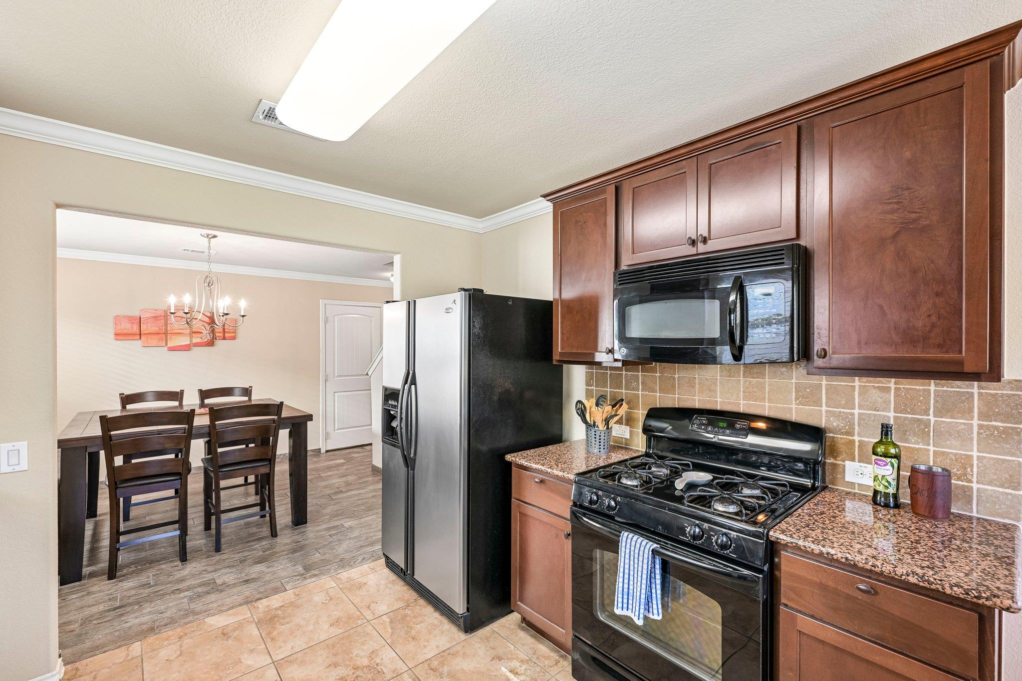 Kitchen with dark wood cabinets and granite counters, opening to a dining area with a chandelier.