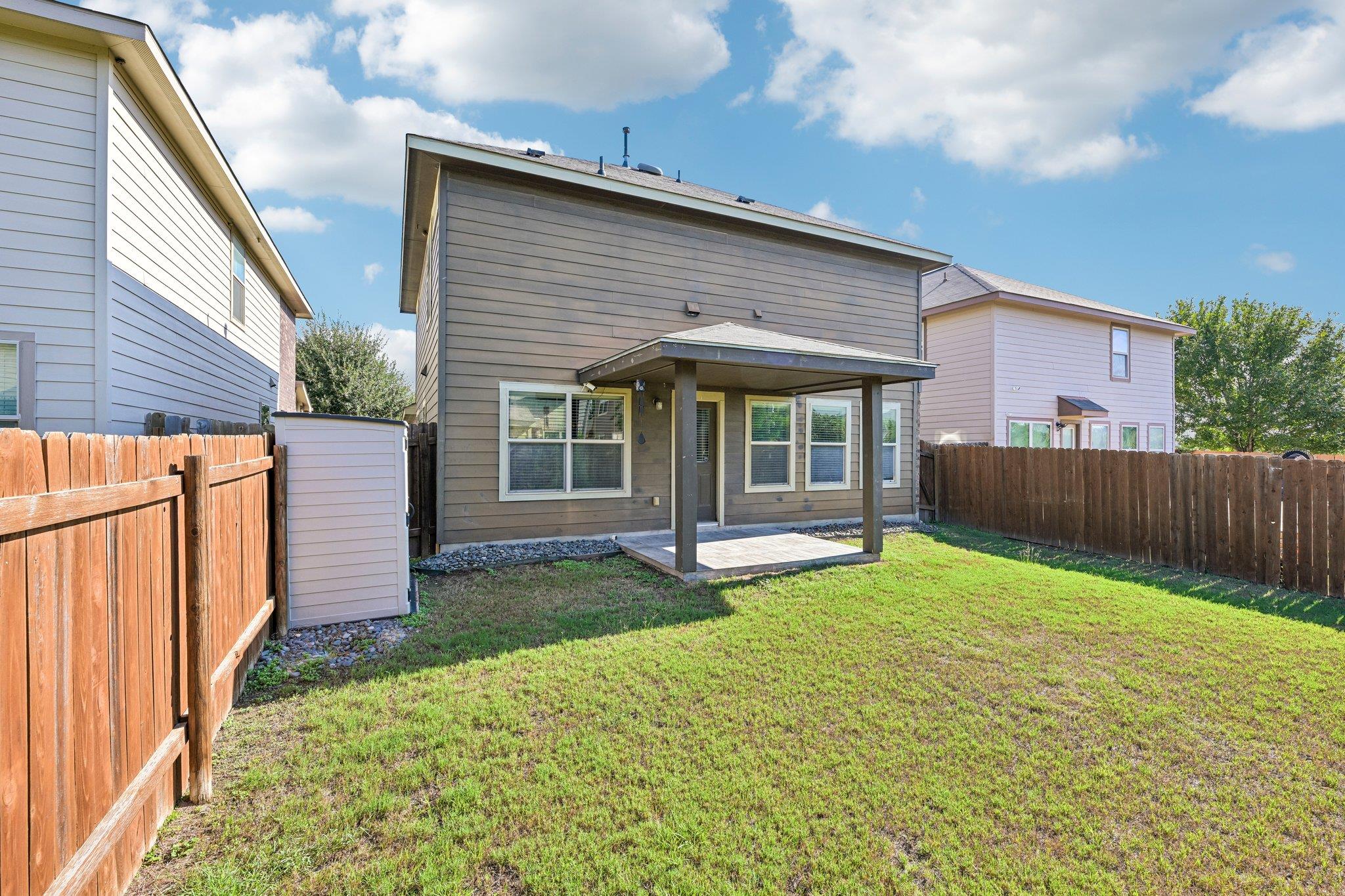 Two-story house with a covered patio opening onto a fenced grassy backyard.