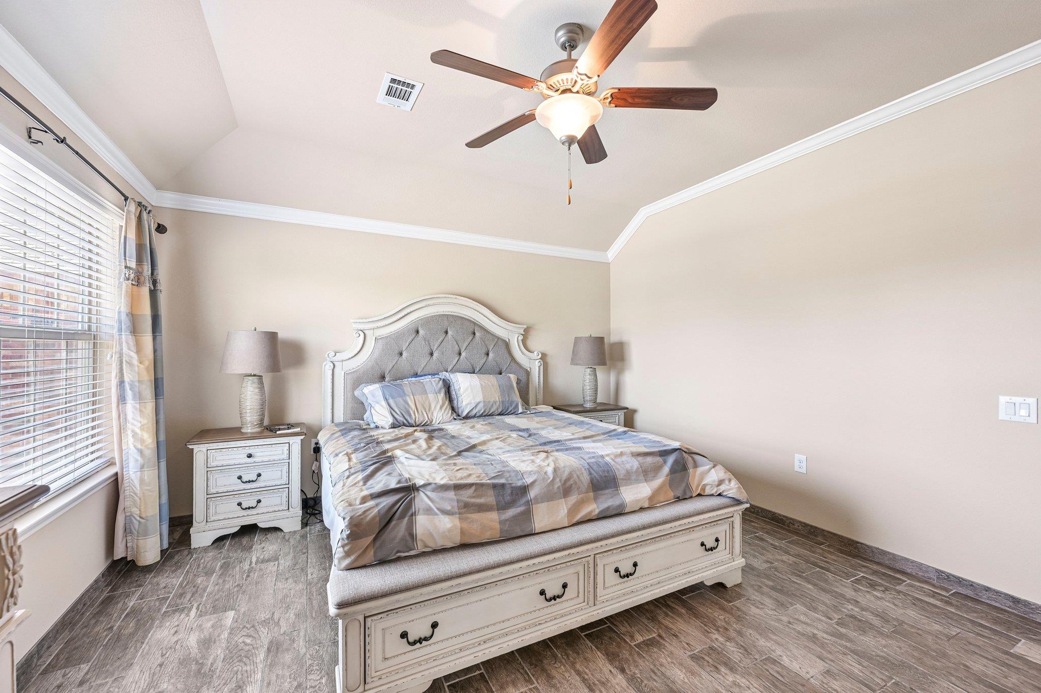 Furnished bedroom with an ornate white bed, plaid bedding, ceiling fan, and dark tile flooring.