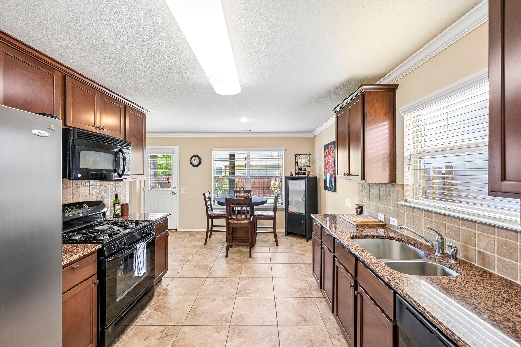 Kitchen with dark wood cabinets, granite counters, stainless appliances, and a dining table by the windows.