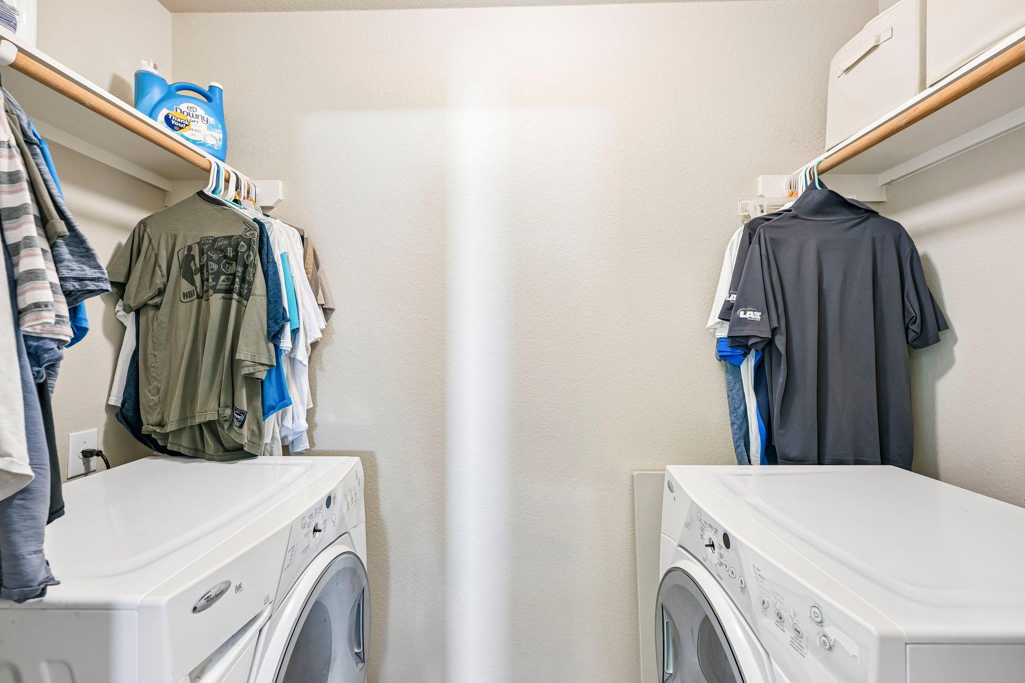 Laundry room with front-loading machines opposite each other and clothes hanging on shelves.