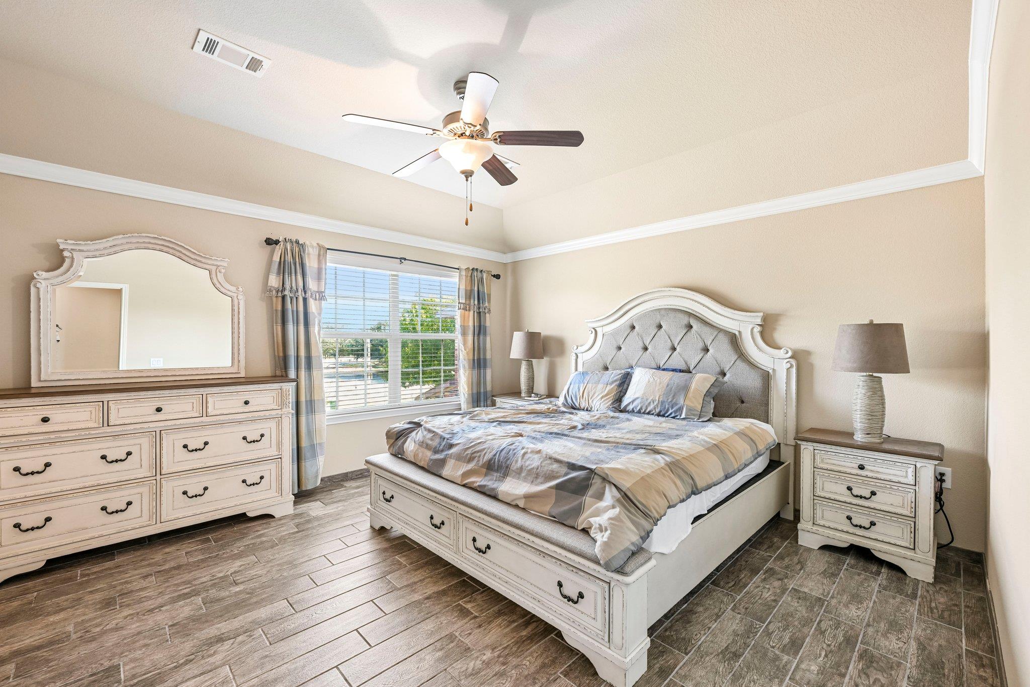 Furnished bedroom with a carved white bed, tufted gray headboard, and matching dresser.