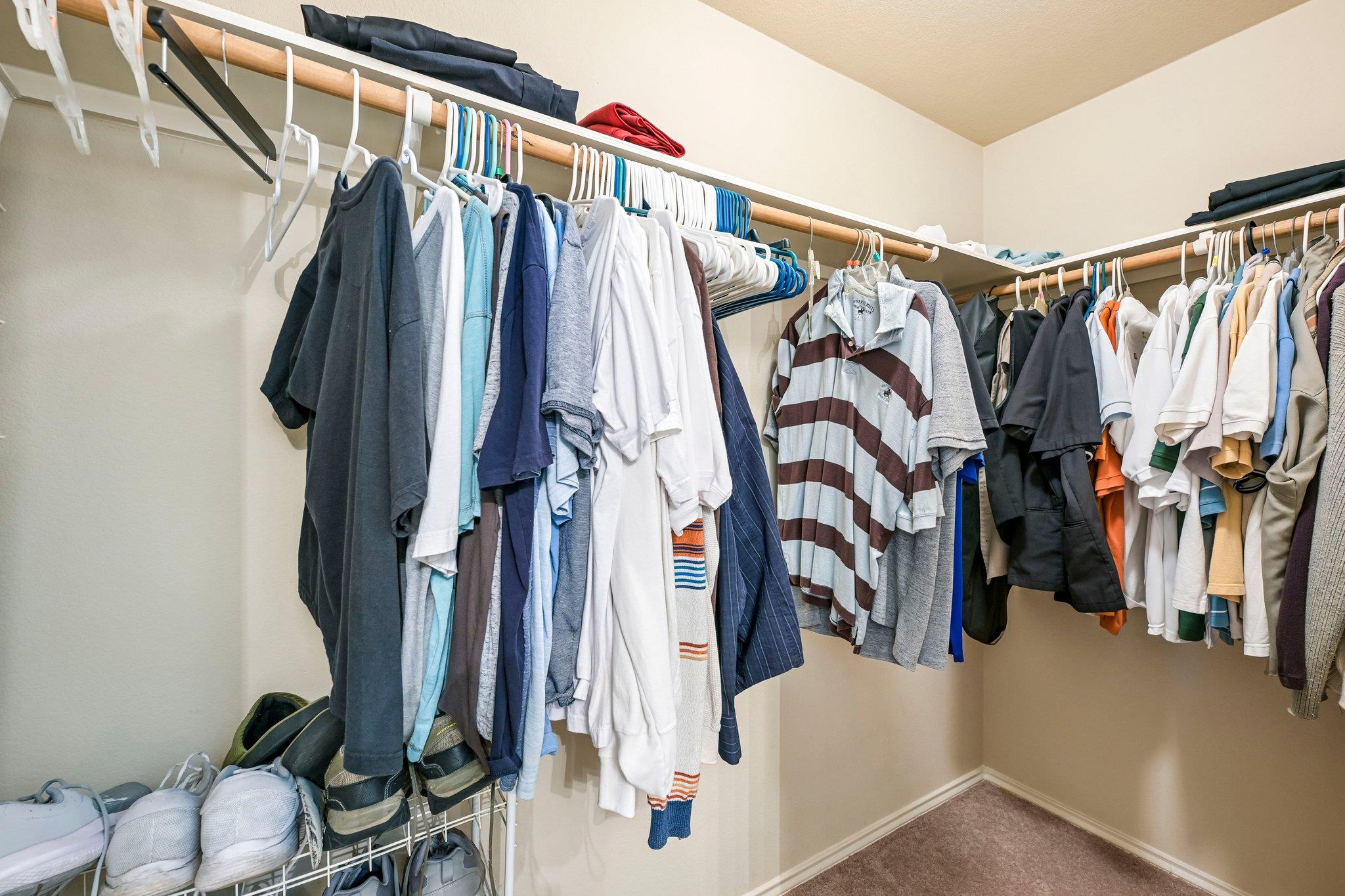 Walk-in closet with clothes on two hanging rails and shoes stored below.