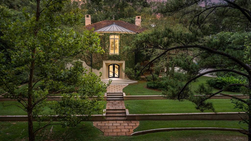 Ivy-covered two-story home framed by mature trees, with a brick walkway leading to its entrance.