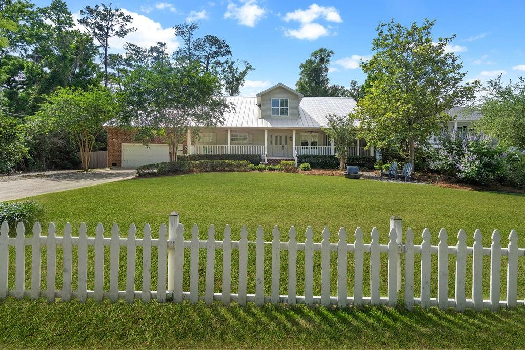 Home with a white metal roof, brick garage, covered porch, and picket fence across the lawn.
